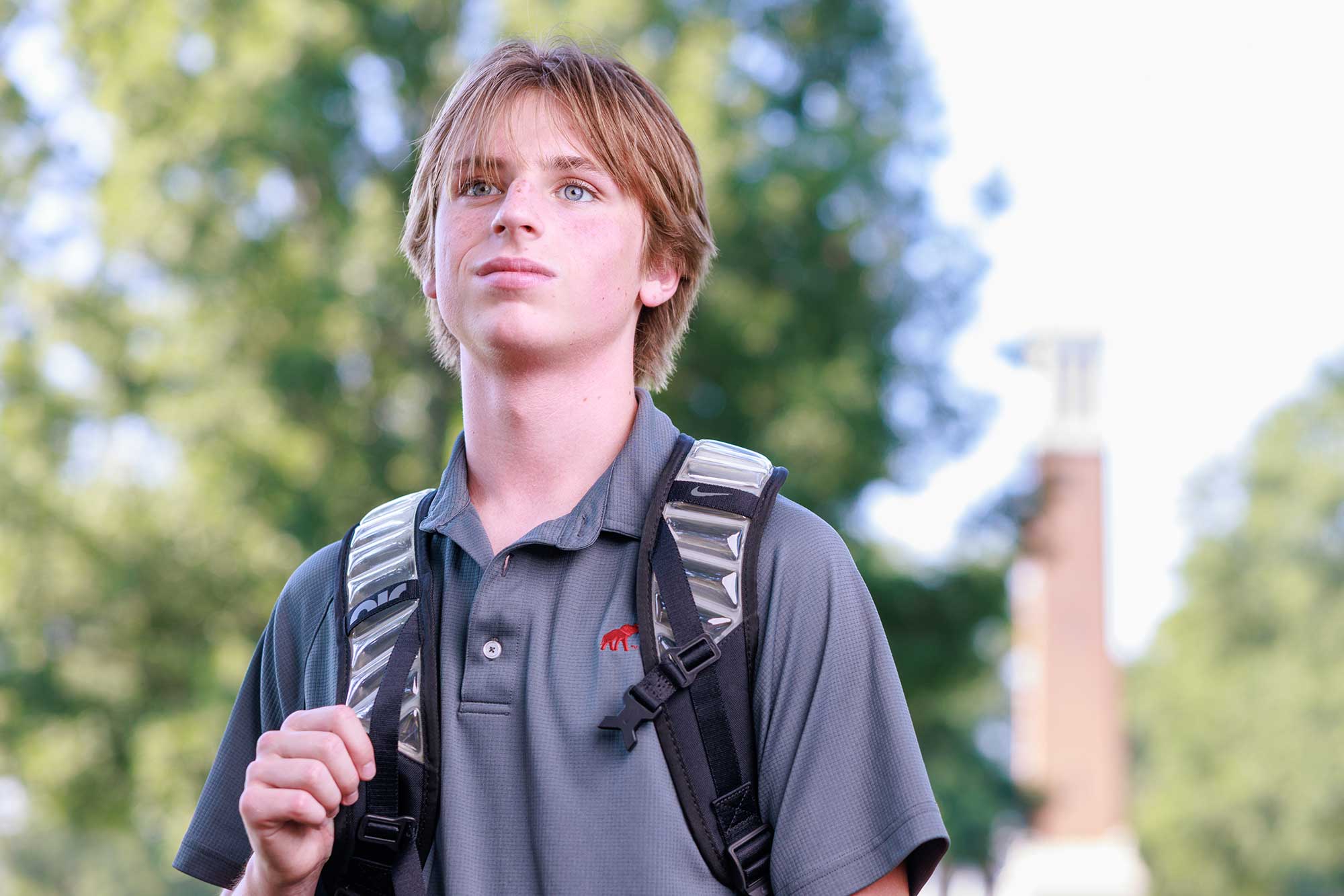 Student holding a backpack standing on the quad.