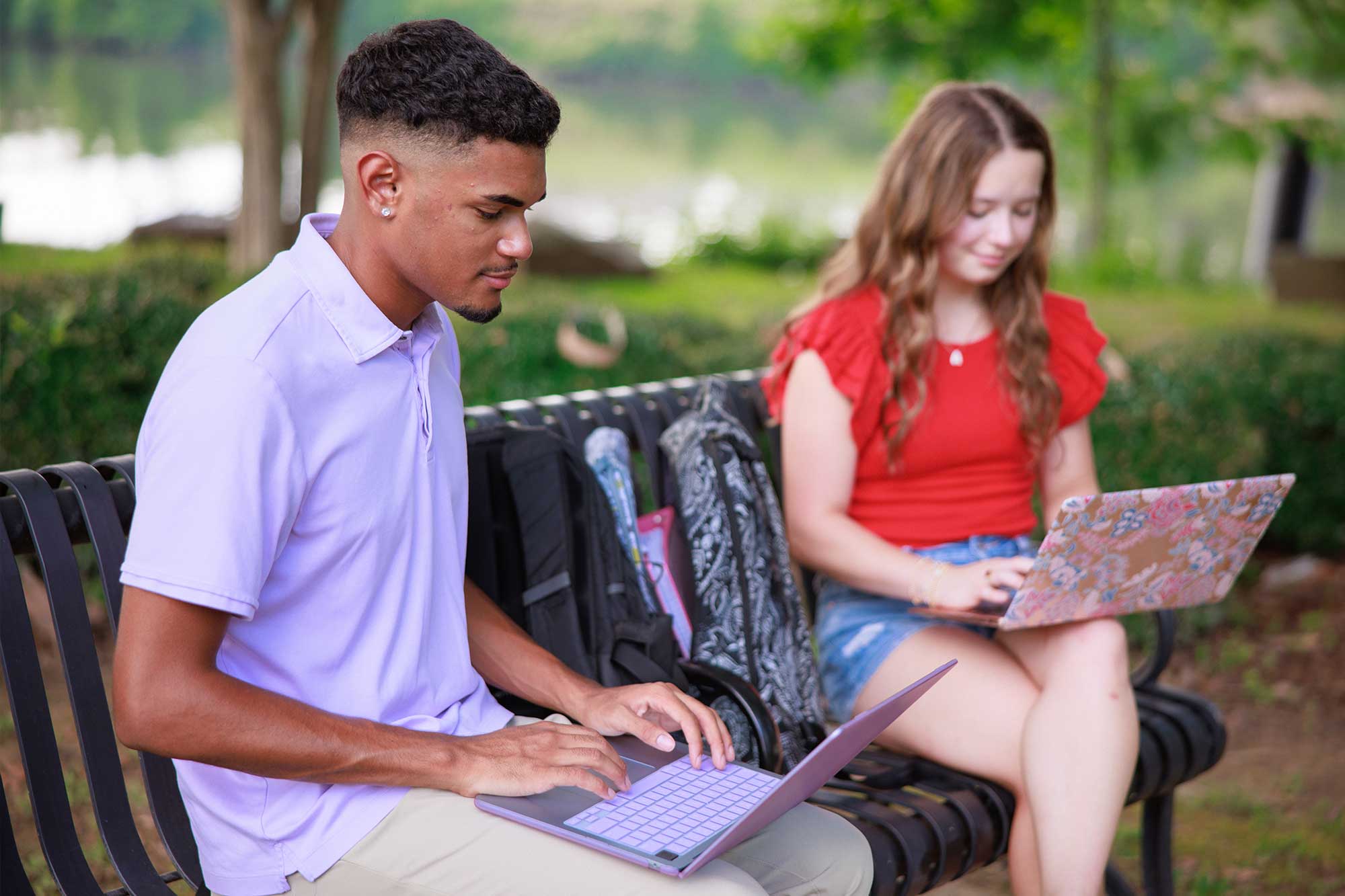 Students sitting on a bench using laptops.